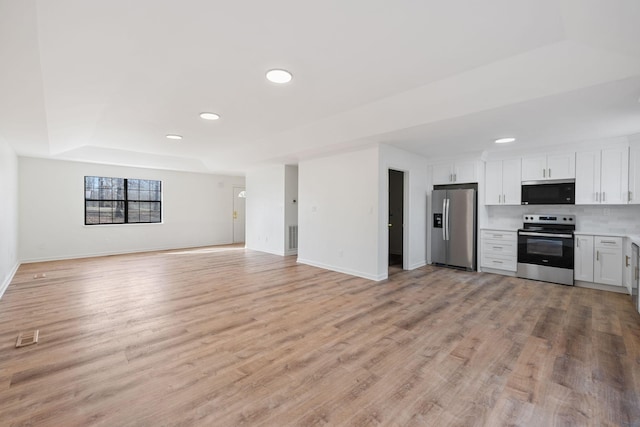 kitchen featuring a tray ceiling, stainless steel appliances, light countertops, light wood-style floors, and open floor plan