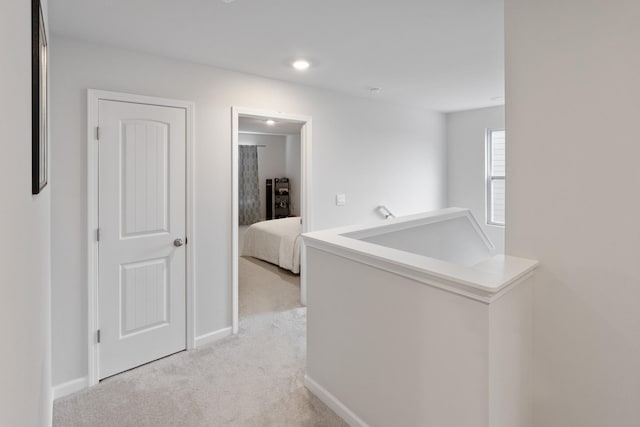 corridor with an upstairs landing, light colored carpet, and baseboards