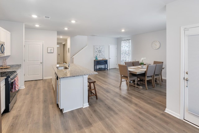 kitchen featuring a breakfast bar, a sink, appliances with stainless steel finishes, white cabinets, and light stone countertops