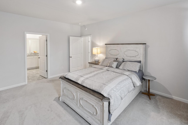 bedroom with baseboards, light colored carpet, and ensuite bath