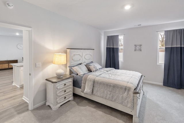 bedroom with baseboards, visible vents, and light carpet