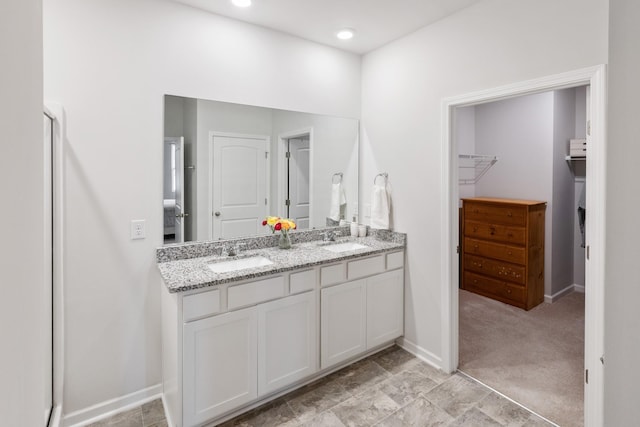 full bath with double vanity, a walk in closet, baseboards, and a sink