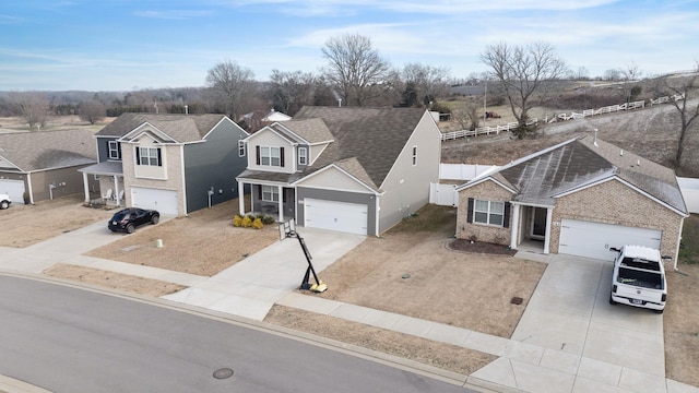 traditional-style home featuring fence, roof with shingles, a residential view, concrete driveway, and brick siding