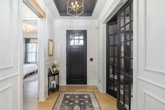 entryway featuring an inviting chandelier, a decorative wall, wood finished floors, and french doors