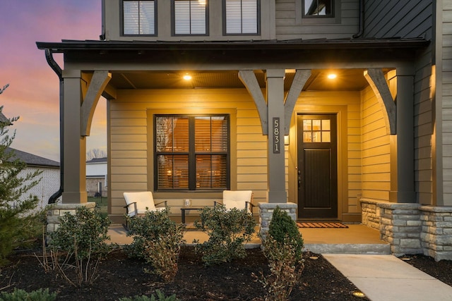 exterior entry at dusk with stone siding and covered porch