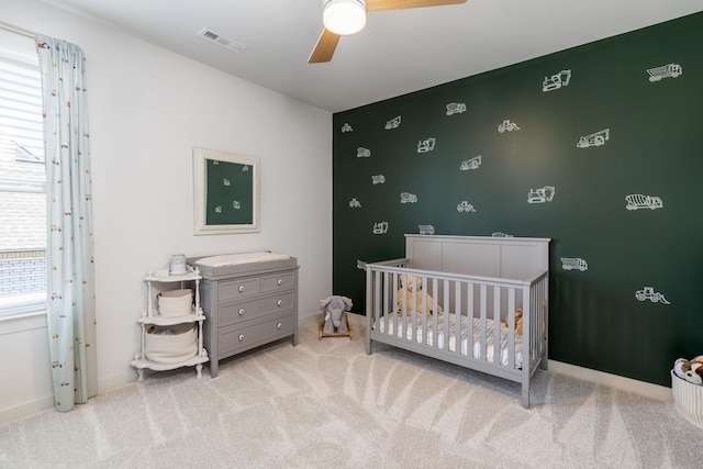 bedroom with visible vents, carpet floors, a nursery area, and a ceiling fan