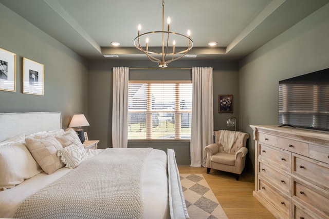 bedroom with a notable chandelier, light wood-type flooring, and a raised ceiling