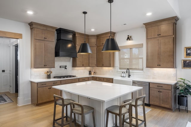 kitchen with a breakfast bar area, light wood-type flooring, appliances with stainless steel finishes, custom exhaust hood, and a sink