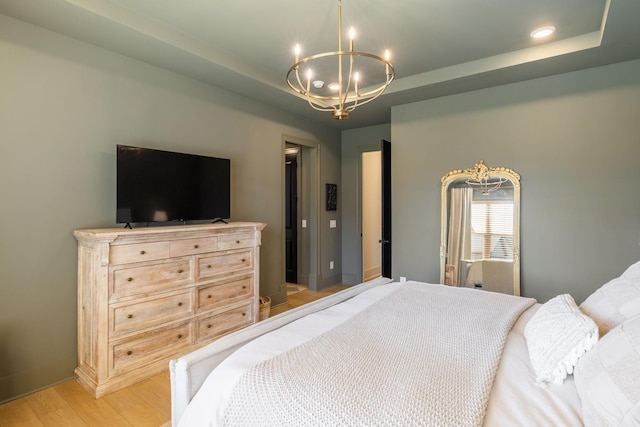 bedroom with an inviting chandelier, baseboards, light wood-style floors, and a tray ceiling