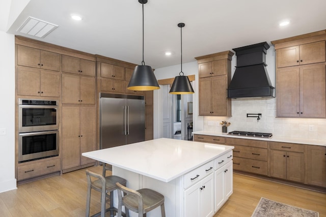 kitchen with stainless steel appliances, custom exhaust hood, visible vents, and light wood-style flooring