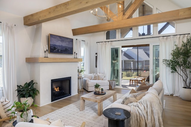 living room featuring a chandelier, beamed ceiling, a lit fireplace, and wood finished floors