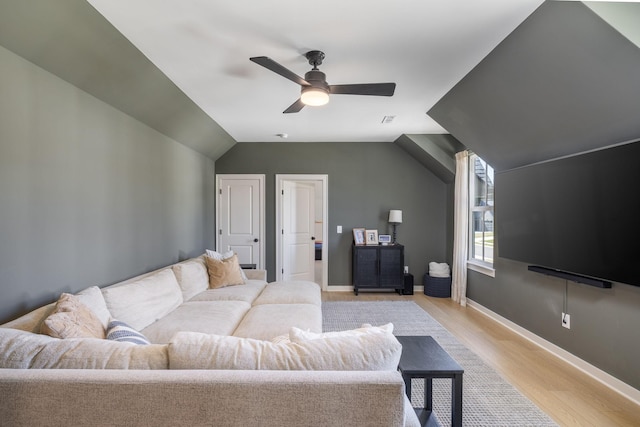 living area with baseboards, a ceiling fan, vaulted ceiling, and light wood finished floors