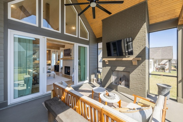 wooden deck with a warm lit fireplace, outdoor dining area, ceiling fan, and a patio