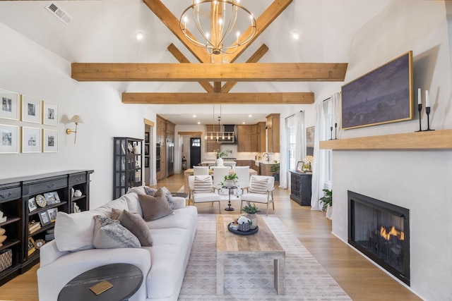 living area featuring light wood finished floors, a notable chandelier, beamed ceiling, and a warm lit fireplace