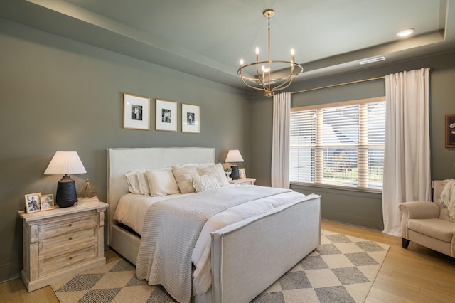 bedroom featuring a raised ceiling, light wood-style flooring, a notable chandelier, and visible vents