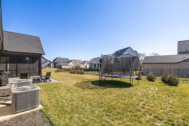 view of yard with central air condition unit, a trampoline, fence, an outdoor fire pit, and a residential view