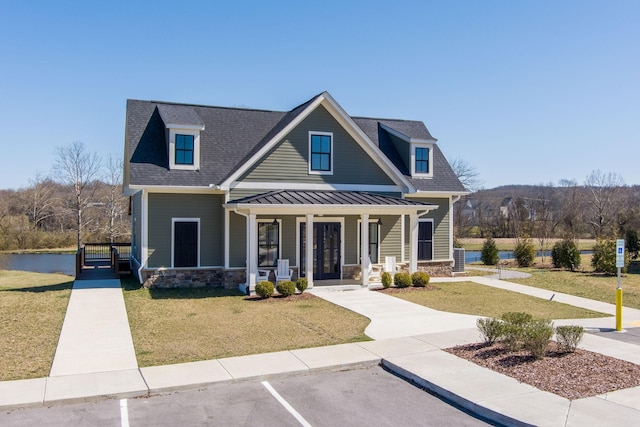 view of front of house featuring a standing seam roof, a porch, a front lawn, stone siding, and metal roof