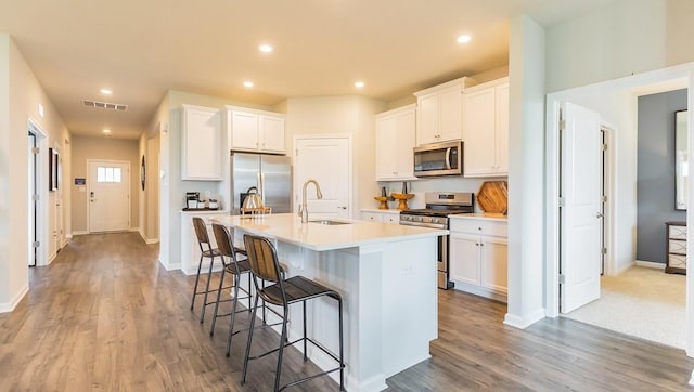 kitchen with a center island with sink, visible vents, a sink, appliances with stainless steel finishes, and a kitchen breakfast bar