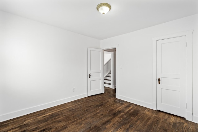 spare room with baseboards and dark wood-style flooring