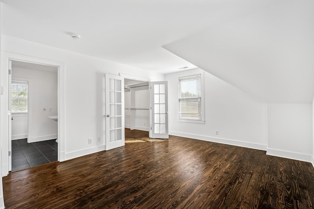 unfurnished bedroom with wood finished floors, french doors, baseboards, a spacious closet, and vaulted ceiling