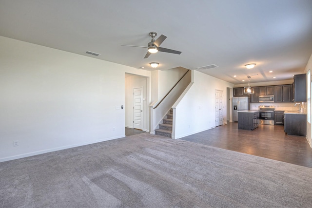 unfurnished living room with stairway, baseboards, visible vents, and dark carpet