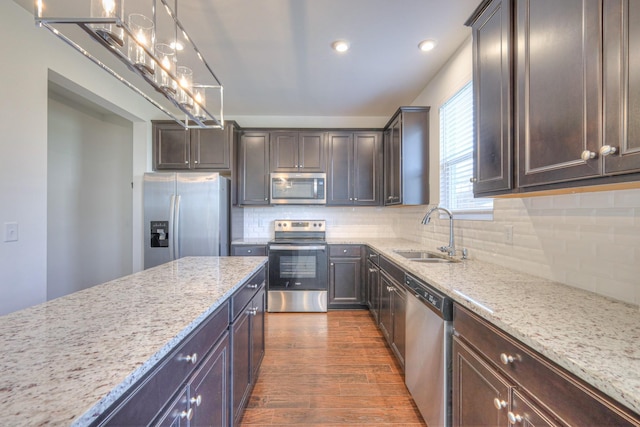 kitchen with dark wood-type flooring, a sink, dark brown cabinetry, appliances with stainless steel finishes, and light stone countertops