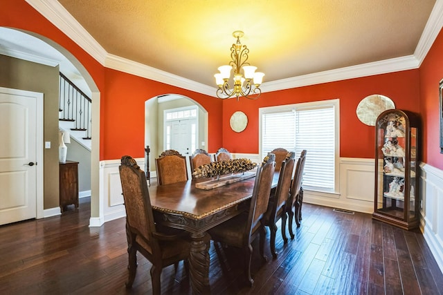 dining space featuring a wainscoted wall, arched walkways, dark wood-type flooring, crown molding, and a notable chandelier