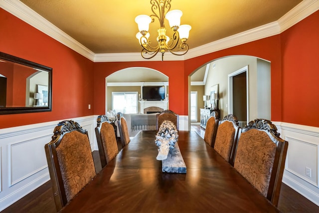 dining room featuring an inviting chandelier, a fireplace, wainscoting, and crown molding