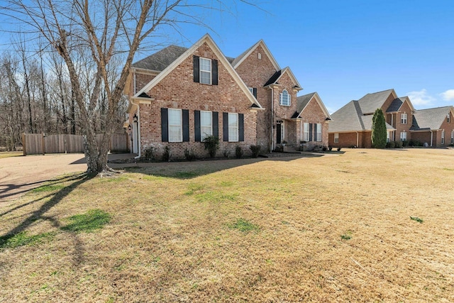 traditional-style home with brick siding, a front lawn, and fence