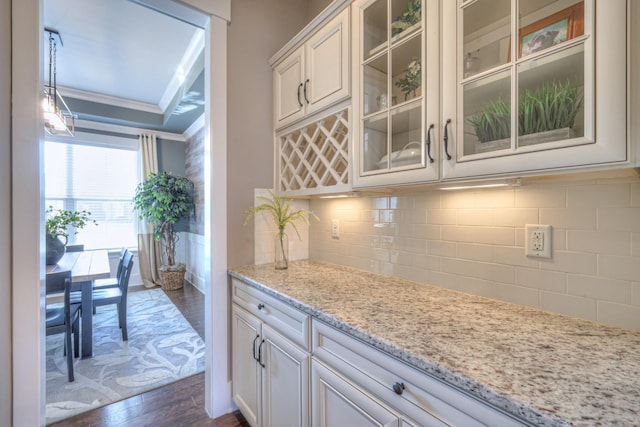 kitchen featuring ornamental molding, light stone counters, tasteful backsplash, glass insert cabinets, and dark wood-style flooring