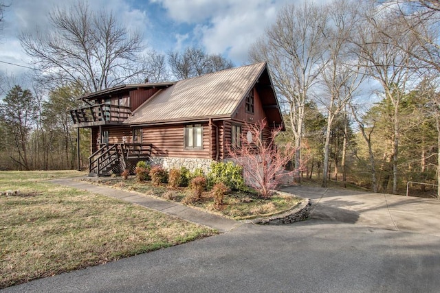 view of home's exterior featuring a balcony, driveway, stone siding, log exterior, and metal roof