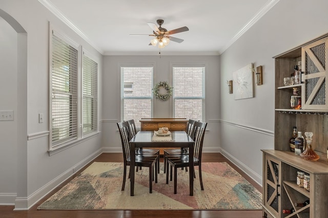 dining room featuring arched walkways, crown molding, baseboards, and wood finished floors