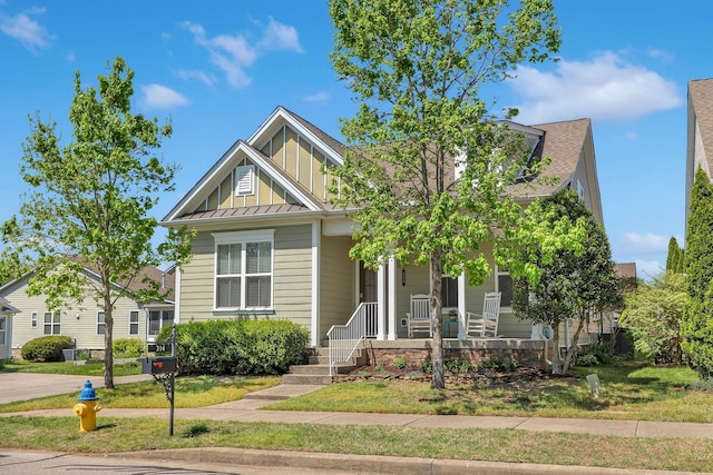 view of front of house with a front yard, a standing seam roof, a porch, board and batten siding, and metal roof