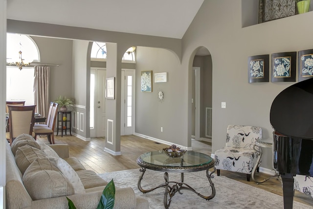 living area featuring visible vents, a chandelier, wood finished floors, arched walkways, and high vaulted ceiling