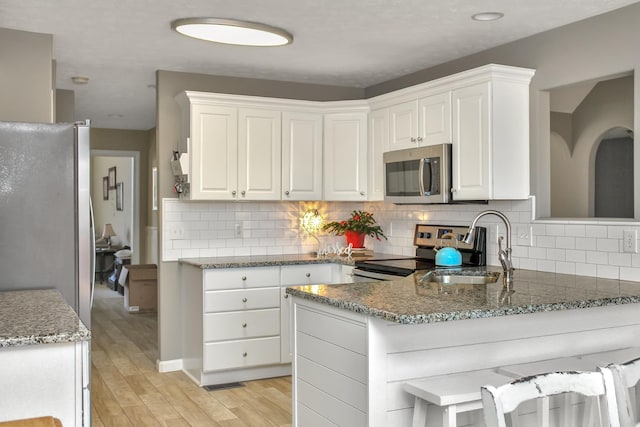 kitchen featuring tasteful backsplash, a peninsula, stainless steel appliances, light wood-style floors, and white cabinetry