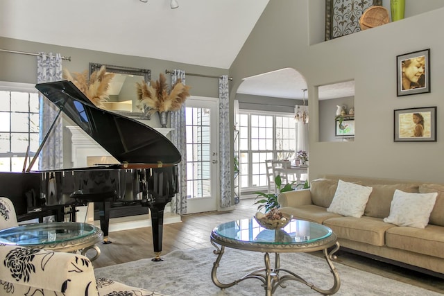 living area featuring arched walkways, high vaulted ceiling, and wood finished floors