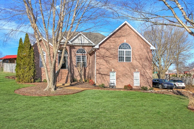 view of front of house with brick siding, a front lawn, and fence