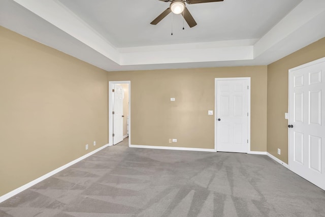 carpeted empty room featuring a raised ceiling, baseboards, and ceiling fan