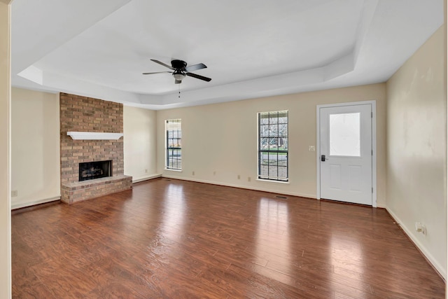 unfurnished living room with a raised ceiling, wood finished floors, a fireplace, baseboards, and ceiling fan