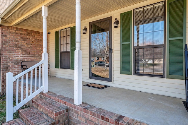 view of exterior entry with brick siding and a porch