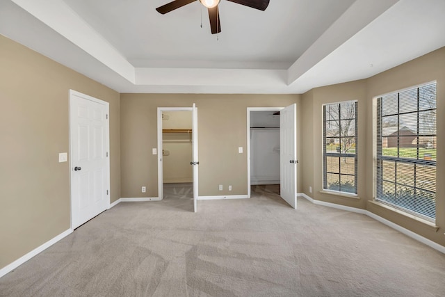 unfurnished bedroom featuring a tray ceiling, baseboards, carpet, and a spacious closet