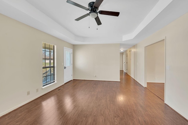 unfurnished room with ceiling fan, baseboards, a raised ceiling, and wood finished floors