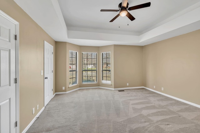 carpeted spare room featuring a tray ceiling, baseboards, and a ceiling fan