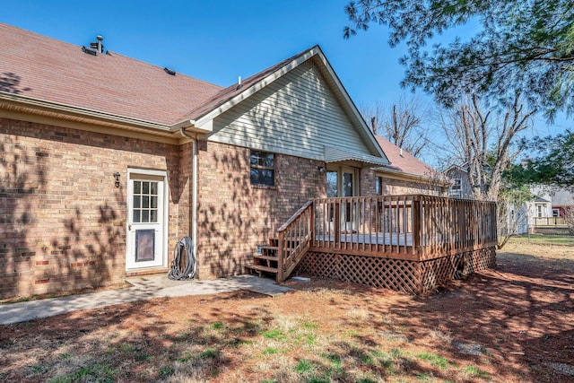 back of property featuring brick siding, a deck, and roof with shingles