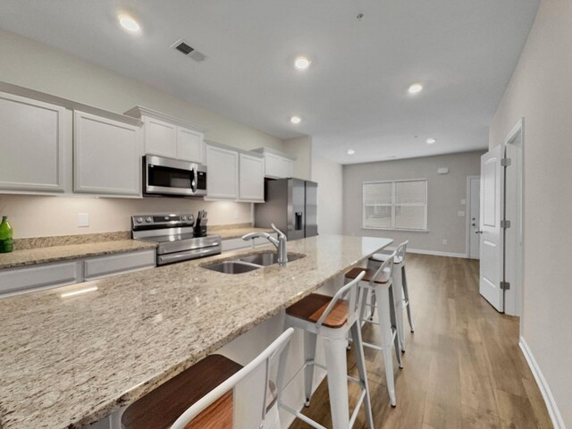 kitchen with a sink, a kitchen breakfast bar, appliances with stainless steel finishes, visible vents, and light wood-style floors
