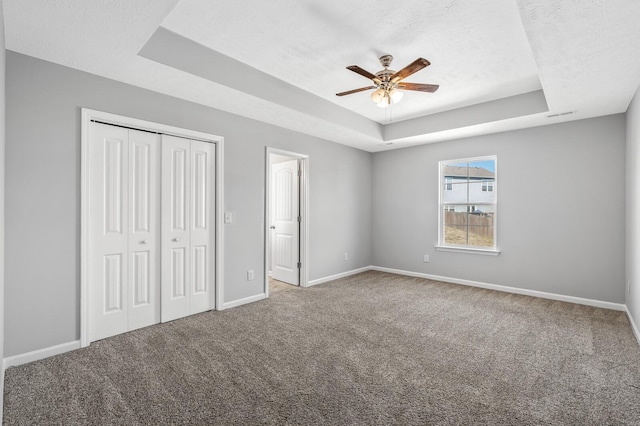 unfurnished bedroom with a raised ceiling, baseboards, carpet floors, and a textured ceiling