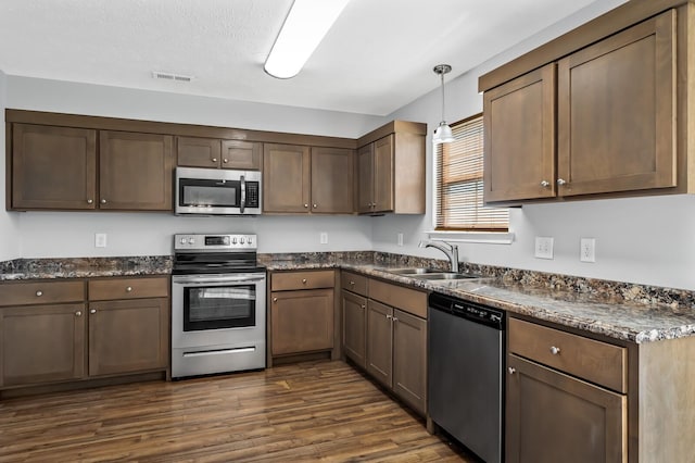 kitchen with visible vents, a sink, stainless steel appliances, dark wood-type flooring, and decorative light fixtures