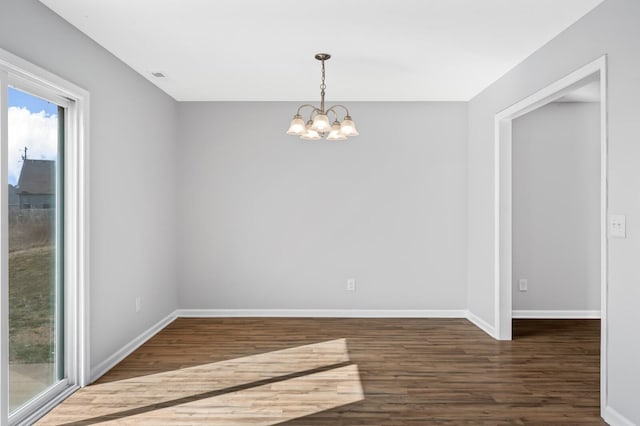 empty room with a chandelier, baseboards, visible vents, and wood finished floors