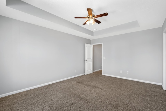 empty room with ceiling fan, carpet, a raised ceiling, and baseboards