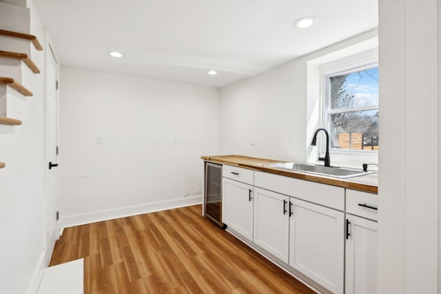 kitchen with open shelves, beverage cooler, butcher block counters, light wood-style flooring, and a sink